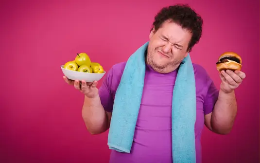 Overweight man trying to make the right choice over a burger and fruit